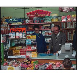 Two men behind shop counter with Cadbury product displays