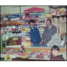 Two men behind shop counter with Cadbury product displays