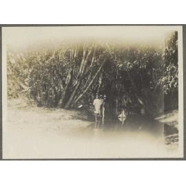 Three children standing in a creek with toy sailing boat
