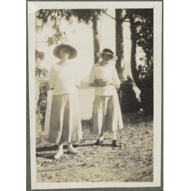 Two unidentified women wearing hats by a fence