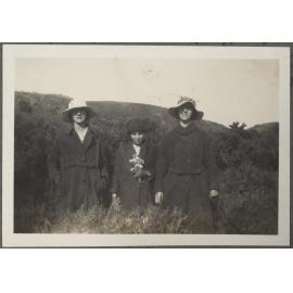 Three women in coats, one holding flowers