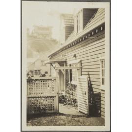 House with trellis and large house on hill in the background 