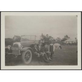Henry, Lesley and Charles Brasch sitting around a car with four other people