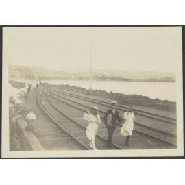One man and two women walking along railway track by a harbour