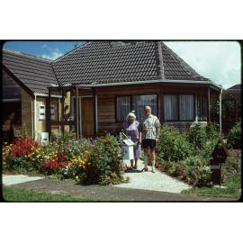 Lady Enid and Sir John Walsh, standing in front of a house