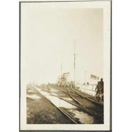 Railway tracks with boys by docked ship flying White Ensign