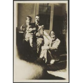 Unidentified man holding a small child, with unidentified woman on a porch