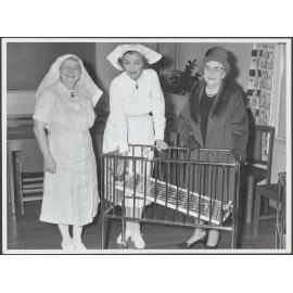 Two nurses and woman with baby cot