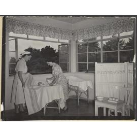 Nurse and mother [?] tucking baby into bassinet