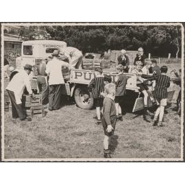 Men unloading crates from the back of a Thomsons truck, surrounded by schoolboys